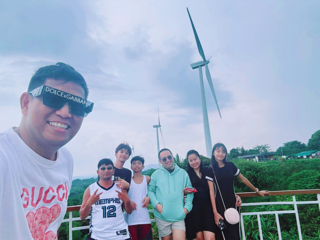 Visitors taking a group photo at Pililla Wind Farm in Rizal, with a wind turbine behind them under a blue sky