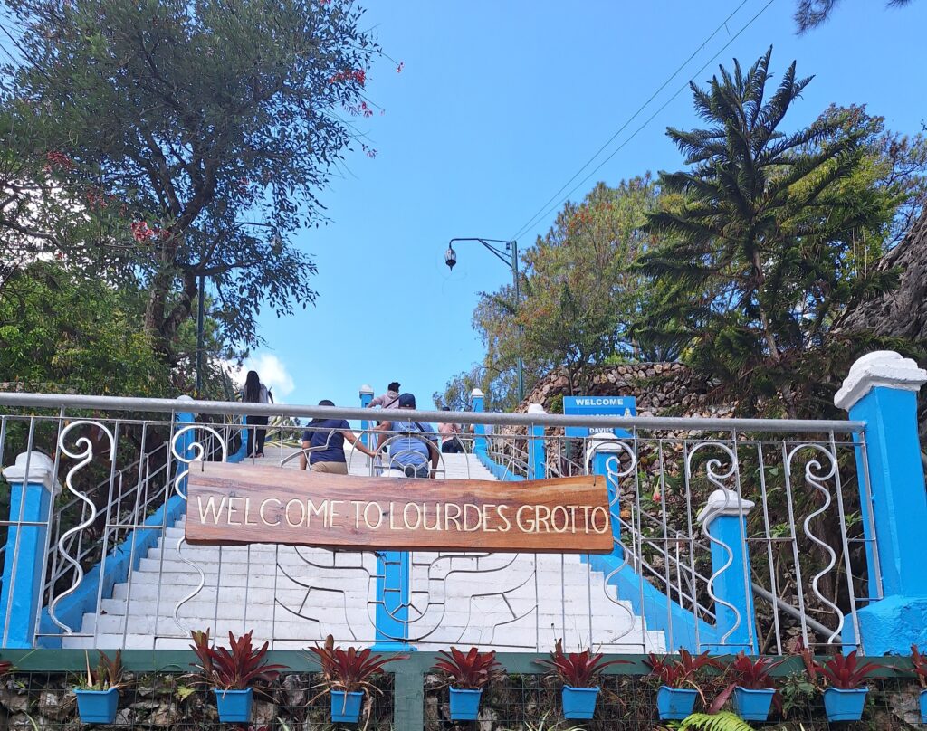 The blue-railed entrance stairway to Lourdes Grotto in Baguio City, with its wooden 'Welcome to Lourdes Grotto' sign