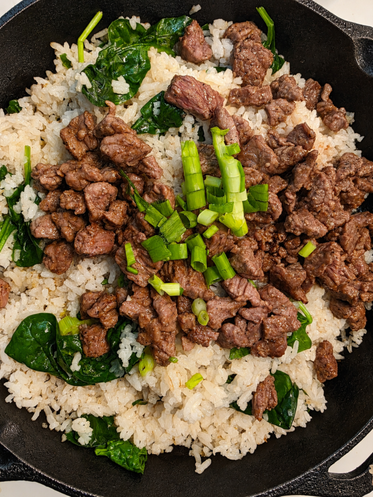 Garlic beef fried rice with marinated beef and spinach in a cast iron skillet