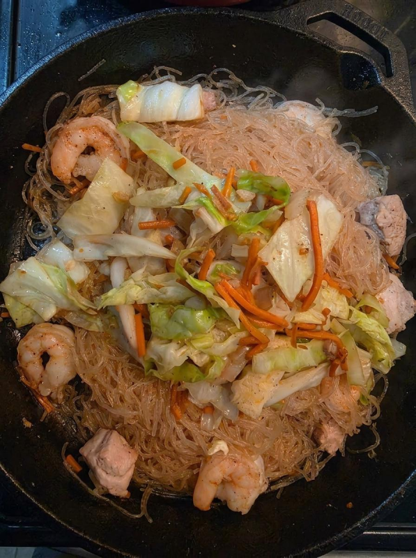 Shrimp pancit bihon with pork, shrimp, cabbage, and carrots in a cast-iron skillet