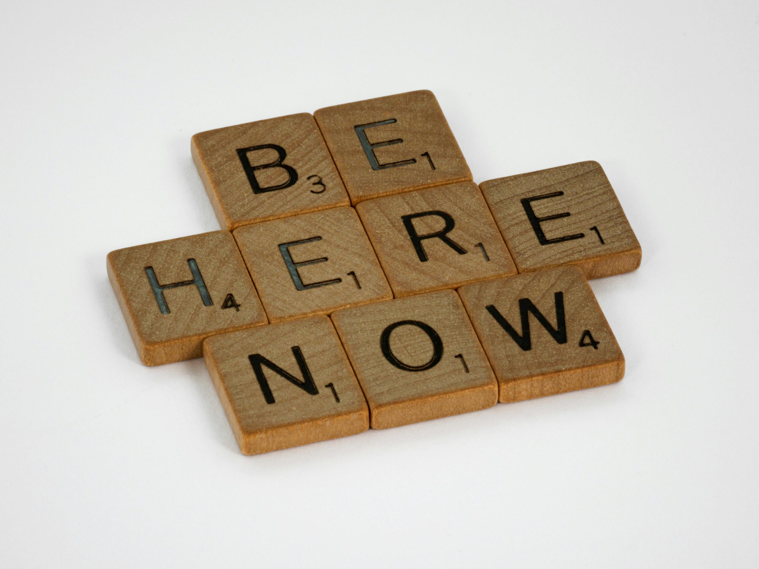 Wooden letter tiles spelling Be Here Now, illustrating The Power of Now by Eckhart Tolle