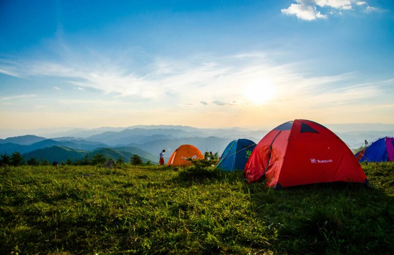 Apiary Mountain Camp in Tanay, Rizal — colorful camping tents on a grassy mountaintop at sunrise with layered mountain views