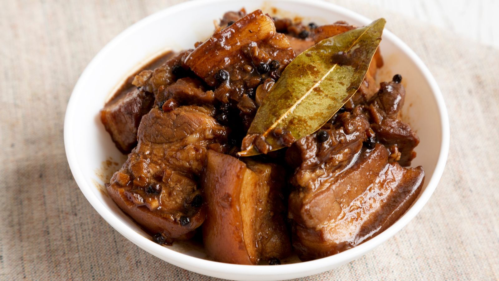 Filipino pork belly adobo in a white bowl garnished with a bay leaf