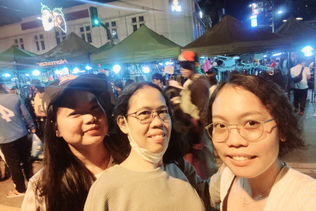 Three friends taking a selfie under the string lights of the Baguio night market on Harrison Road